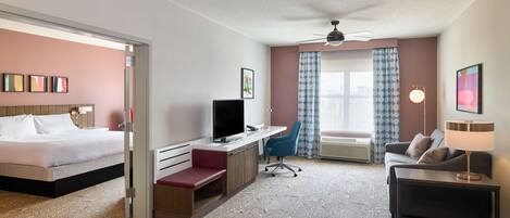 Una habitación de hotel con cama, escritorio, silla, sofá y ventilador de techo.