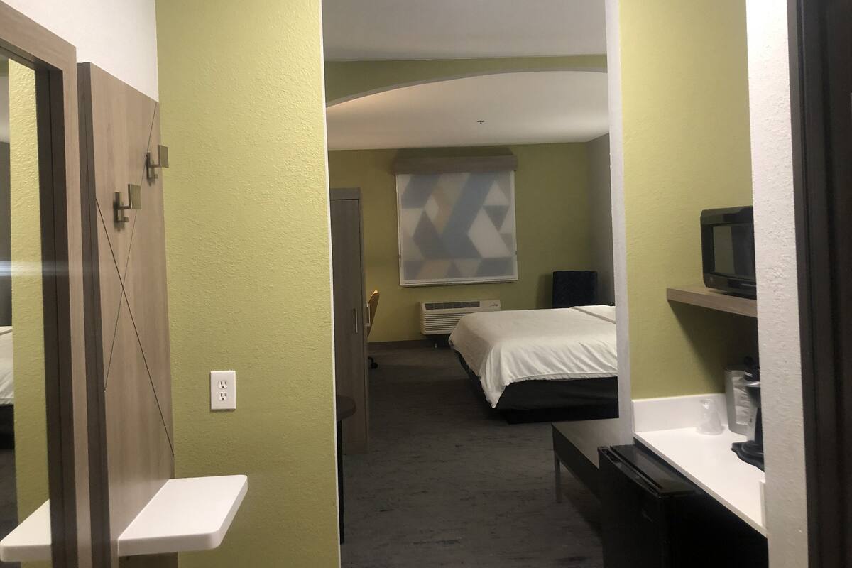 A hotel room with a bed, a TV, a small table, and a window with a geometric pattern.