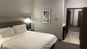A hotel room with a large bed, a nightstand with a phone, a painting on the wall, and a door leading to another room. - Holiday Inn Express & Suites Woodward by IHG (Woodward)