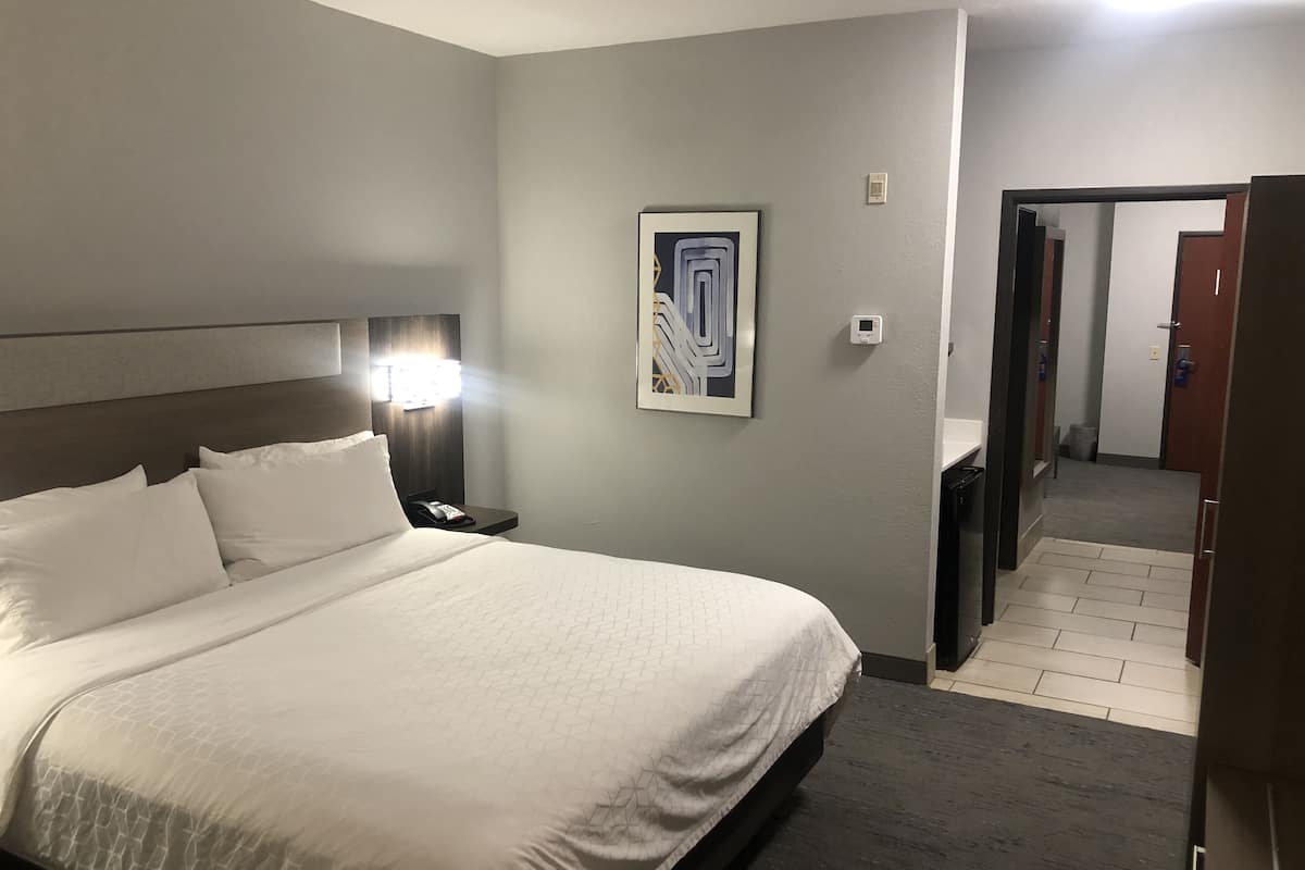 A hotel room with a large bed, a nightstand with a phone, a painting on the wall, and a door leading to another room.