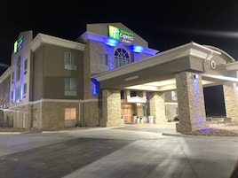 Um hotel Holiday Inn Express & Suites com fachada de pedra, entrada coberta e placa indicando altura livre de 4,4 metros.