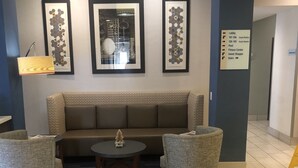 A lobby area with a sofa, two chairs, a coffee table, and a sign indicating guest room locations. - Holiday Inn Express & Suites Woodward by IHG (Woodward)