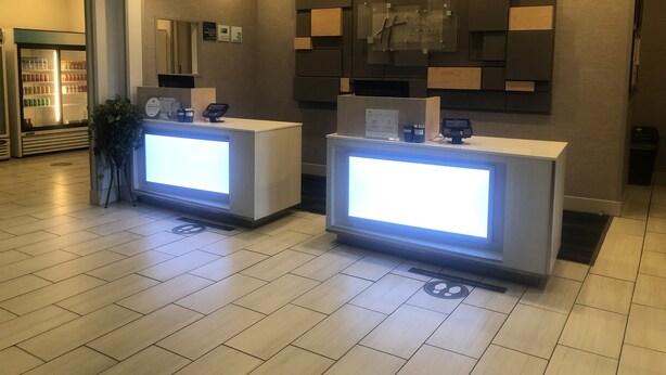 A reception area with two reception desks, a refrigerator with beverages, and a wall-mounted sign. - Holiday Inn Express & Suites Woodward by IHG (Woodward)