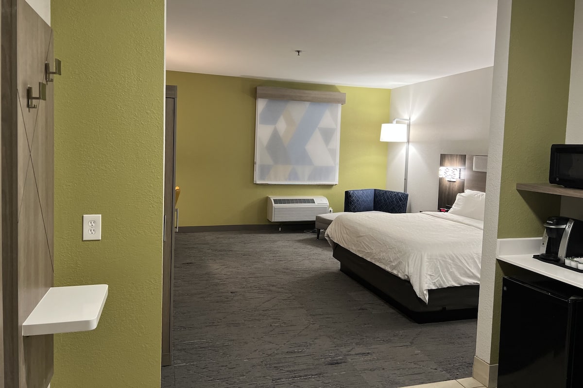 A hotel room with a bed, a desk, a chair, a lamp, and a wall-mounted TV.