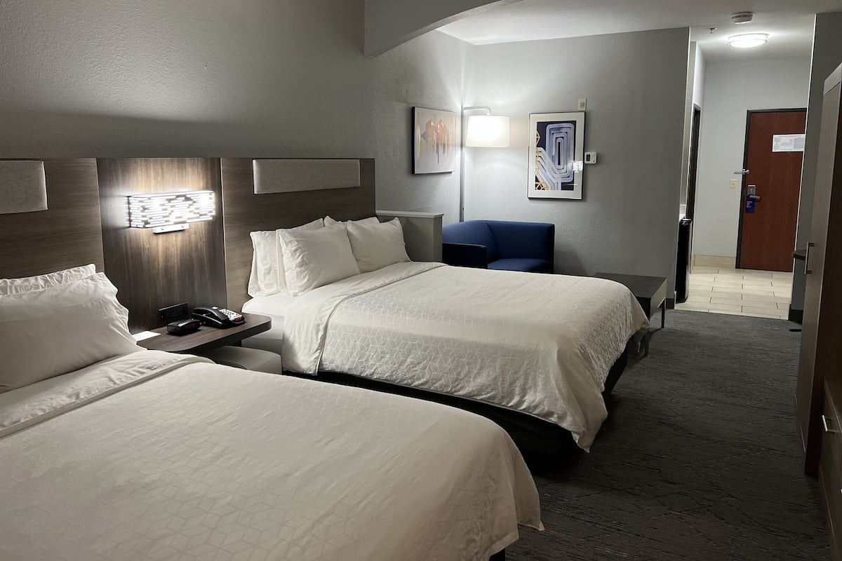 A hotel room with two beds, a desk with a phone, a chair, and artwork on the walls.