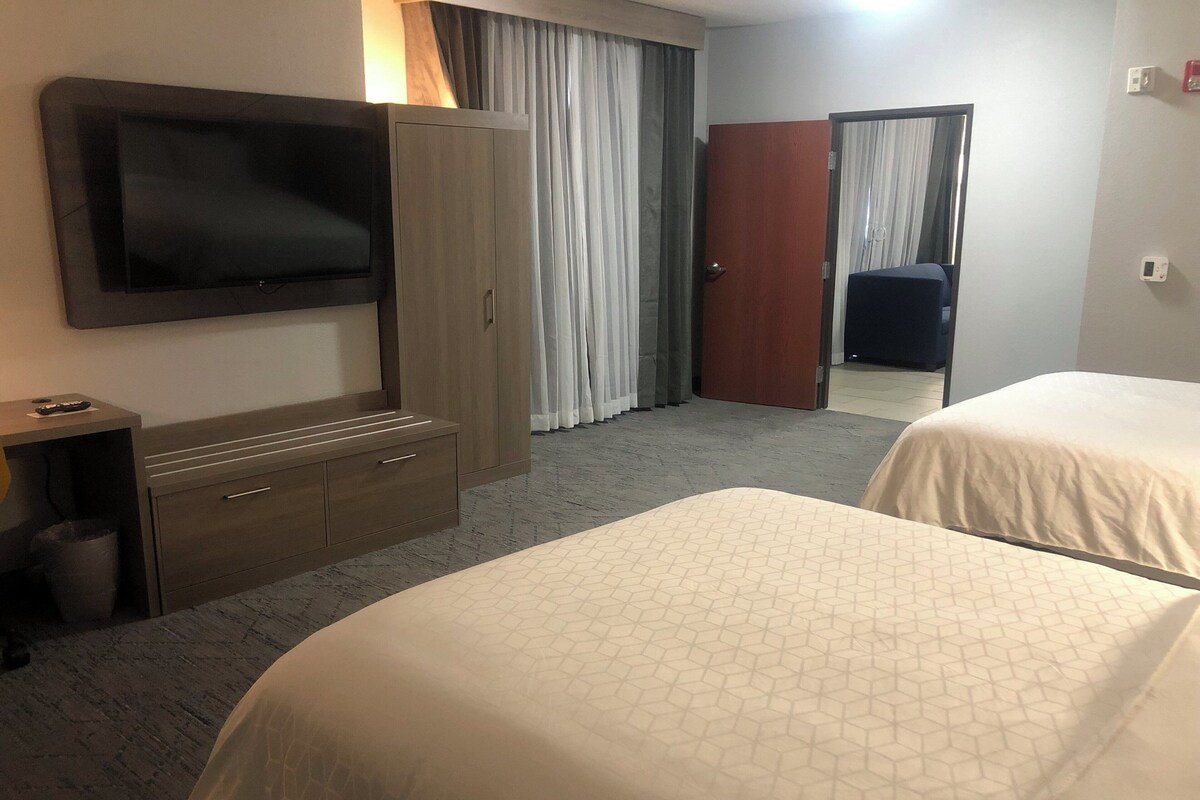 A hotel room with two beds, a TV, a wardrobe, and a desk.