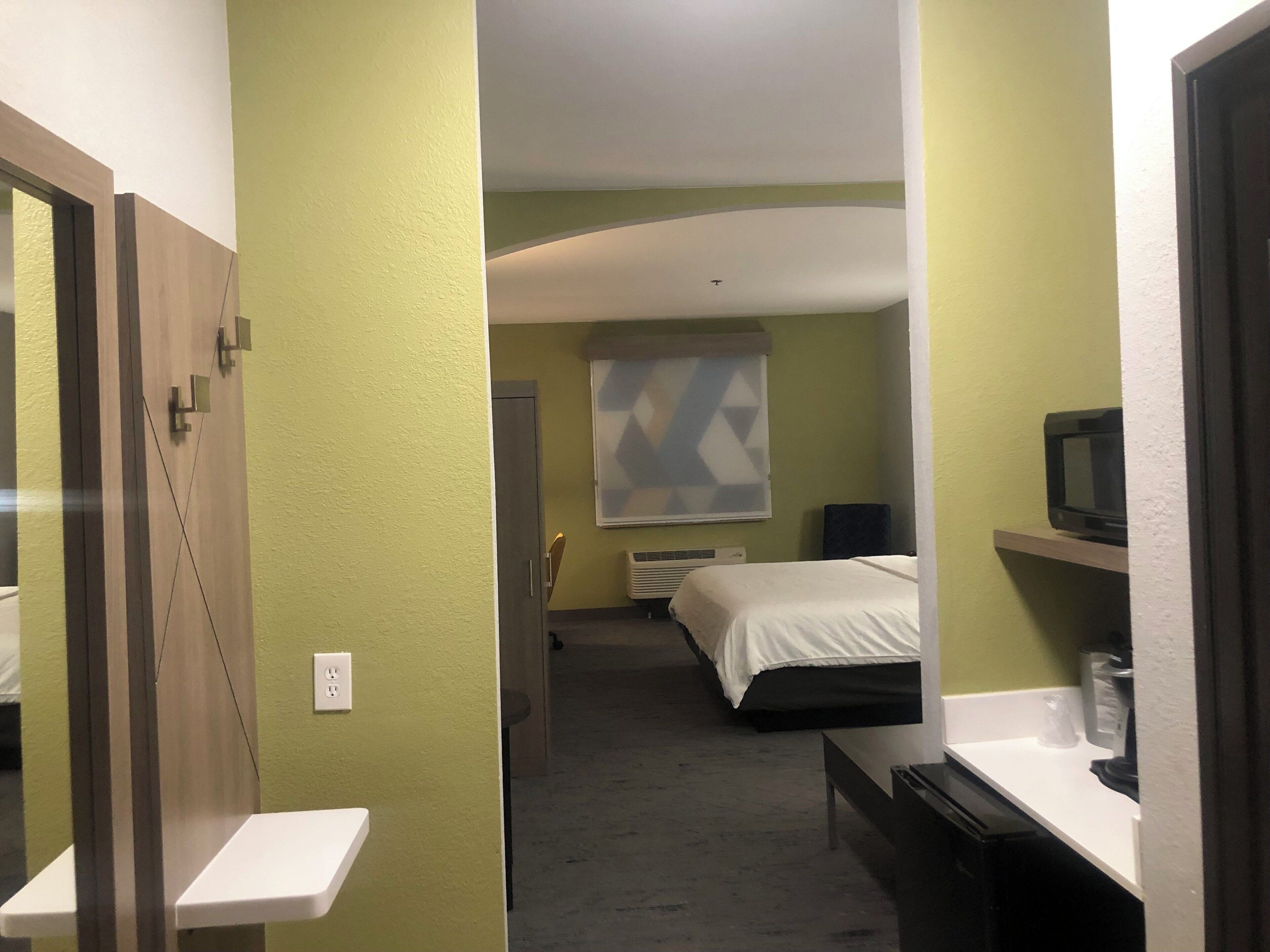 A hotel room with a bed, a TV, a desk, and a window with blinds.