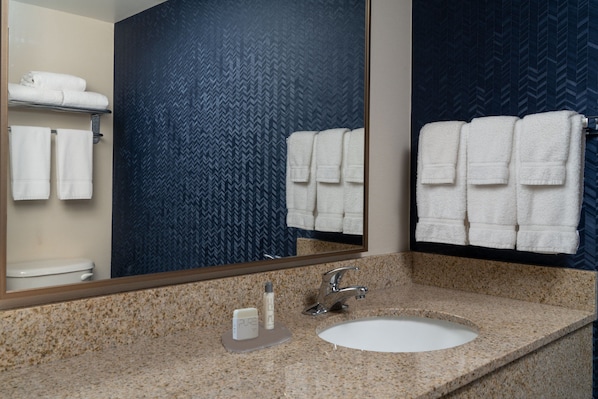 Un baño con encimera de granito, un lavabo blanco, un espejo y toallas en un perchero.