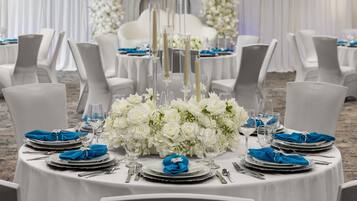 Mesa redonda dispuesta para un evento formal, con arreglos florales blancos, cristalería transparente y servilletas azules.