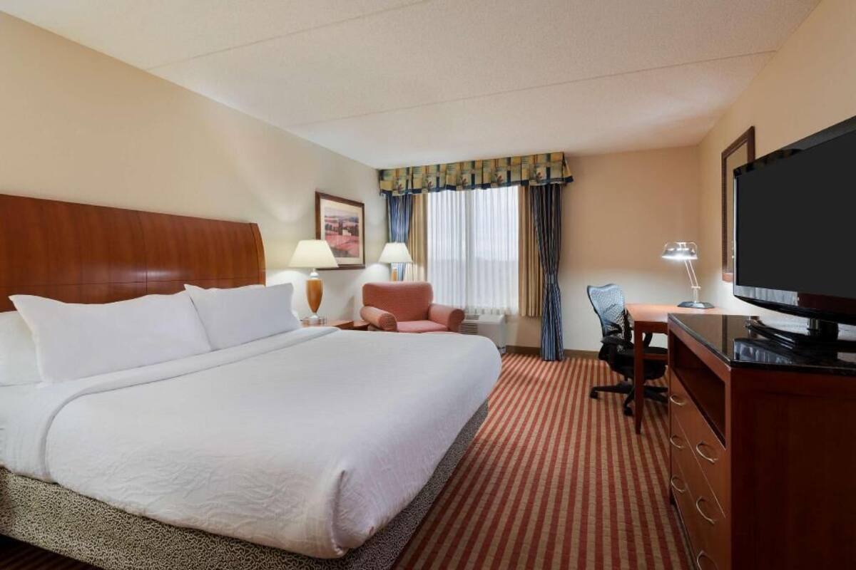 A hotel room with a large bed, a desk with a computer, a television, and a chair.