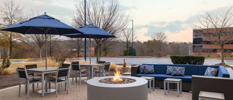 Un espace extérieur aménagé en terrasse, avec des sièges, un foyer et des parasols.