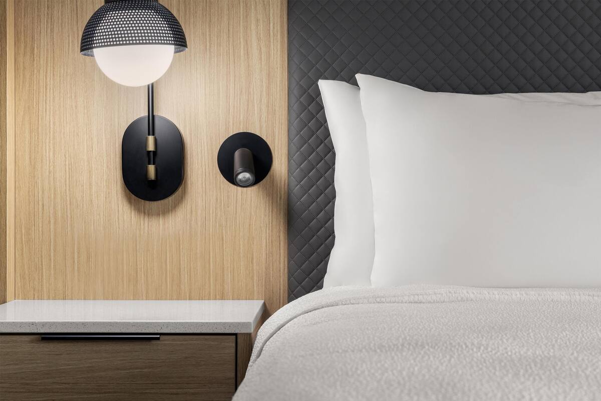 A modern bedroom with a wooden wall, a black and white lamp, a quilted headboard, and a white bed.