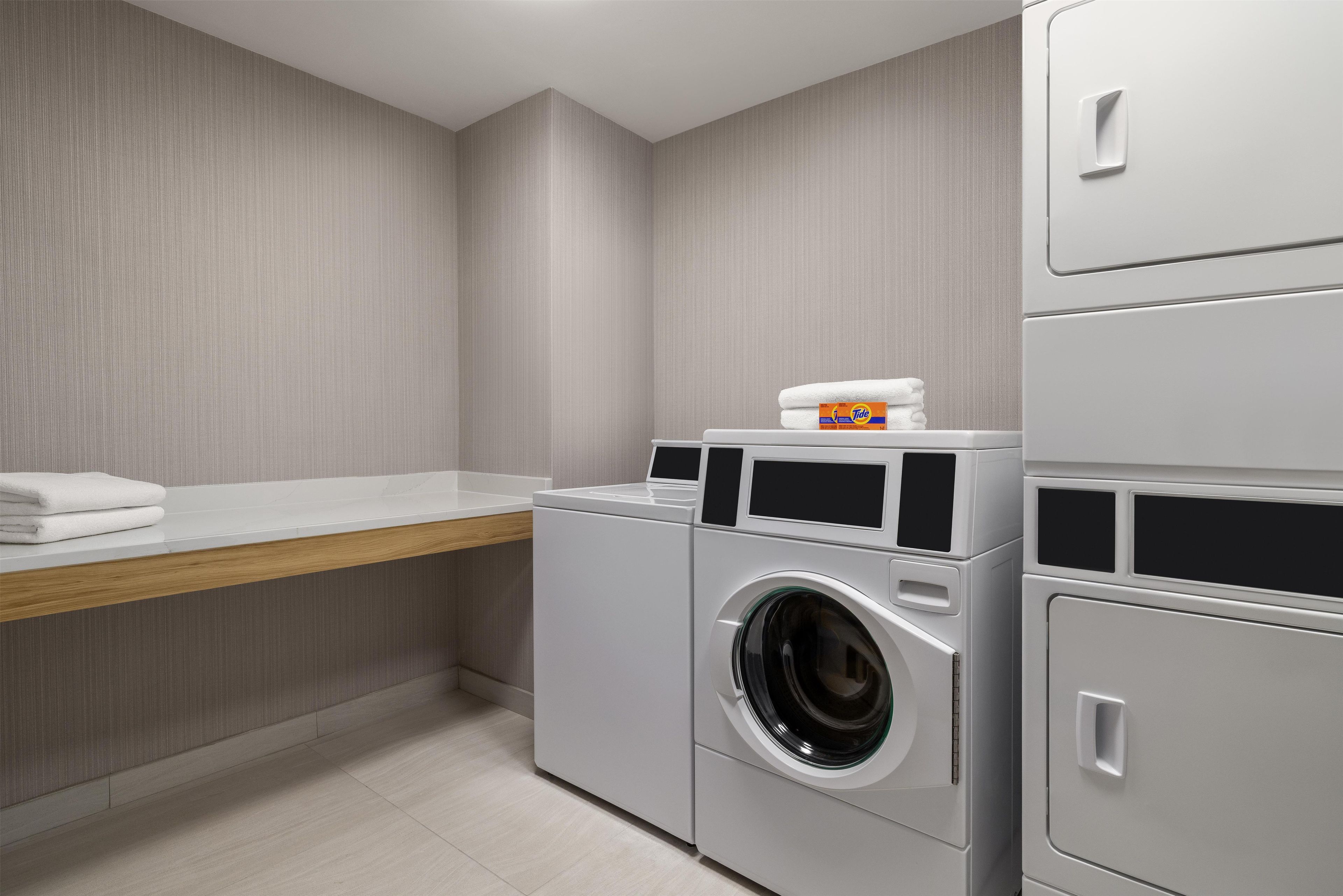 A laundry room with a washing machine, a dryer, and a shelf with folded towels.