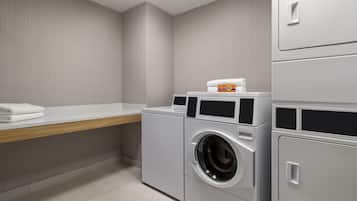 A laundry room with a washing machine, a dryer, and a shelf with folded towels.