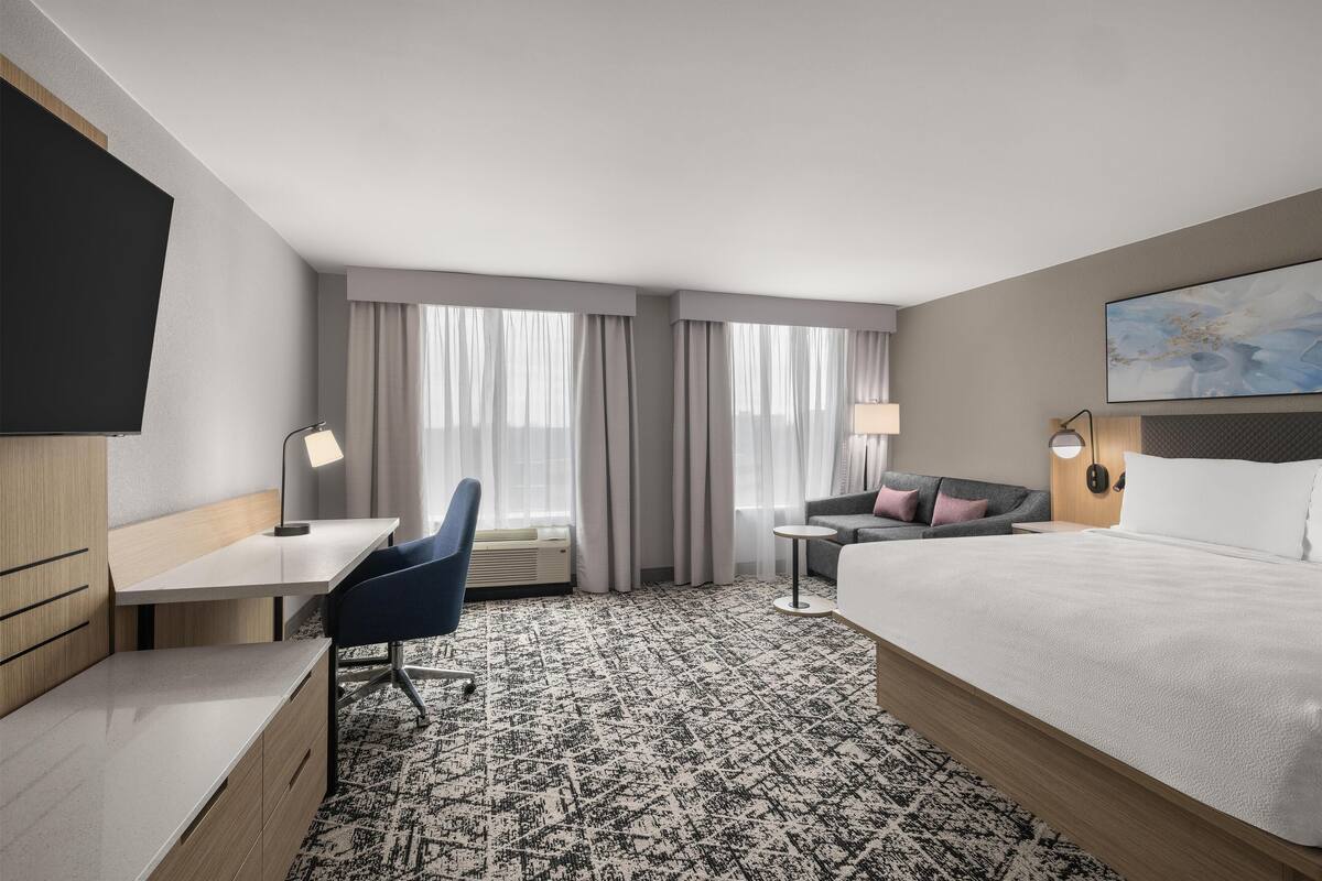 A hotel room with a bed, desk, chair, and a TV.