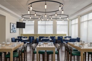 Un restaurante con varias mesas y sillas, un televisor de pantalla plana en la pared y amplios ventanales.