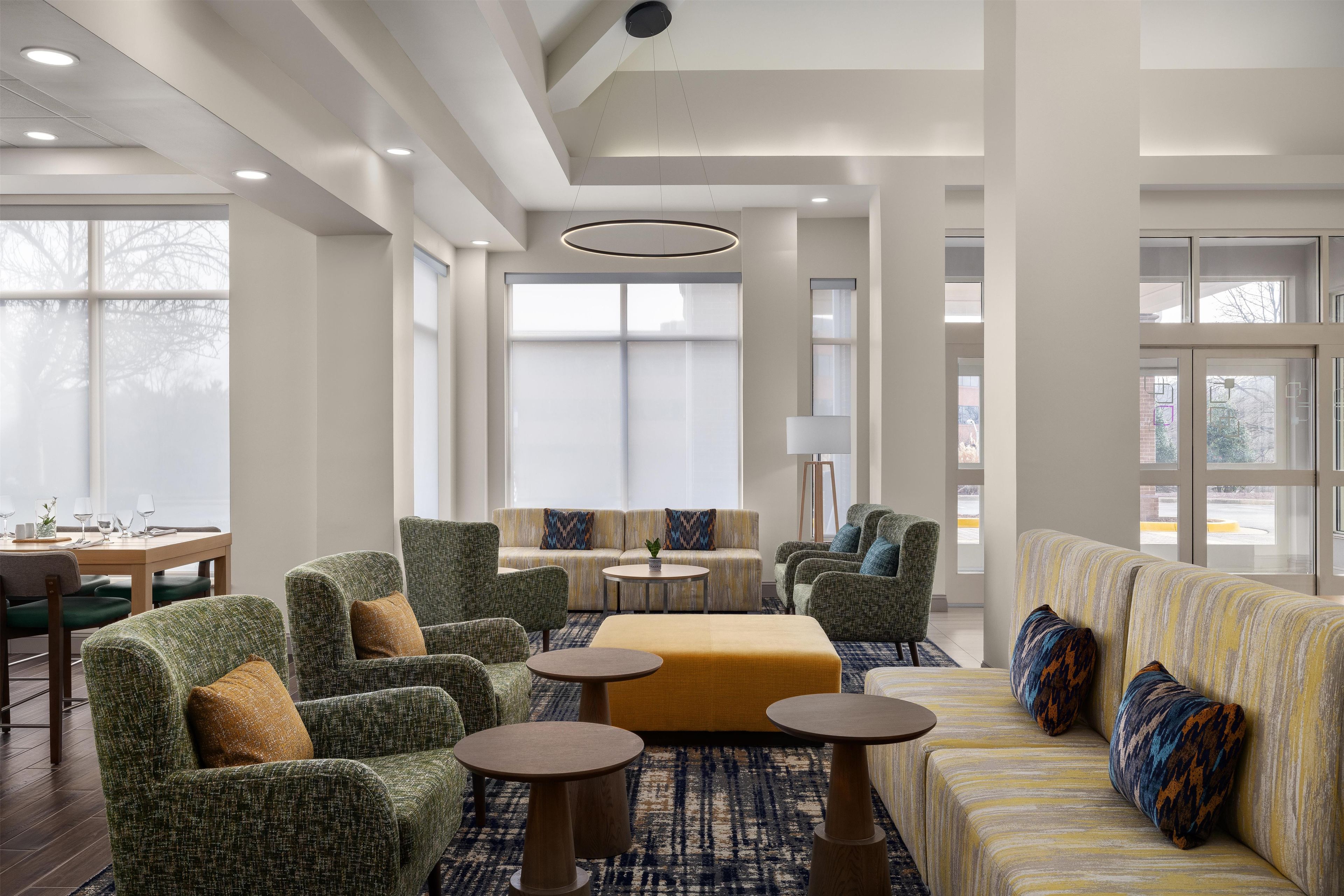 Een ruime hotelentree met een hoge plafond, grote ramen en een zithoek met banken en fauteuils.