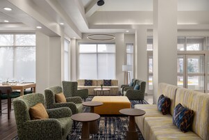 Un amplio vestíbulo de hotel con techo alto, ventanas grandes y una zona de estar con sofás y sillones.