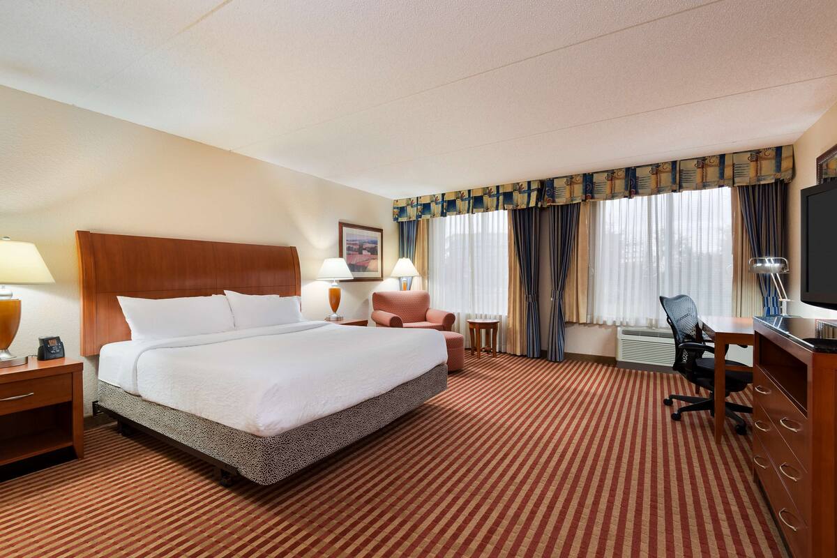 A hotel room with a large bed, a desk, a chair, and a TV.