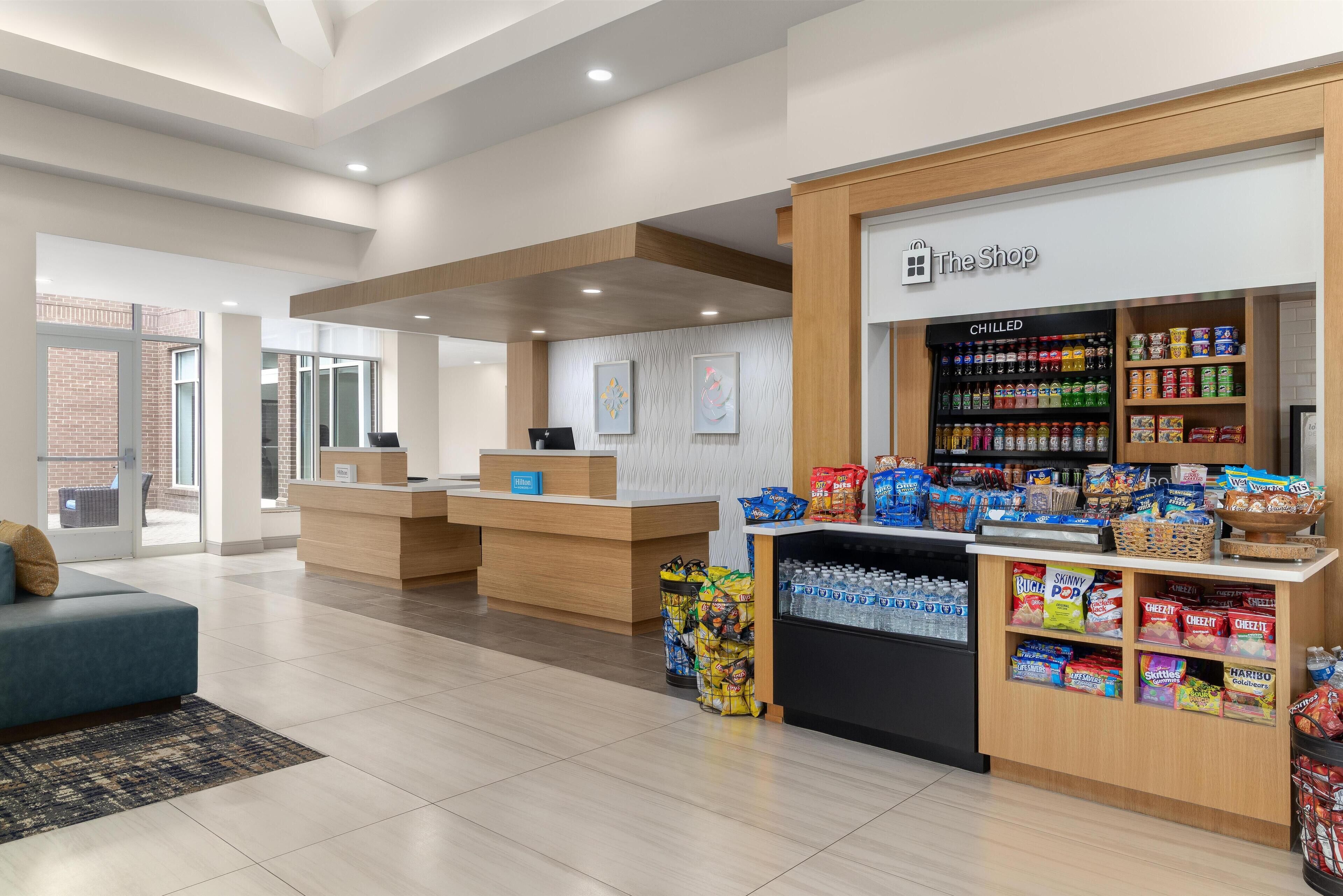 A modern hotel lobby with a reception desk, seating area, and a snack bar.