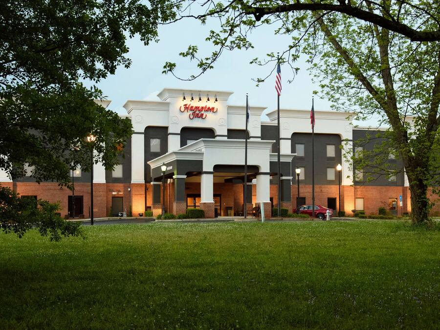 A Hampton Inn hotel with a modern facade, a flagpole, and a well-maintained lawn.
