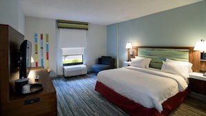 Une chambre d’hôtel avec un grand lit, un bureau avec une télévision, une chaise, une fenêtre et un mur décoré de motifs colorés.