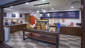 Un espace dédié au petit-déjeuner, avec un sol à carreaux, une table centrale où sont disposés les aliments, et un tableau noir servant de menu, accroché au mur.