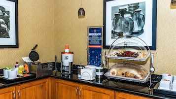 Montaje de bufé con una máquina para hacer gofres, una cafetera y una mesa de exhibición de alimentos.