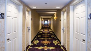 A hotel hallway with carpeted floors, white doors, and overhead lighting.