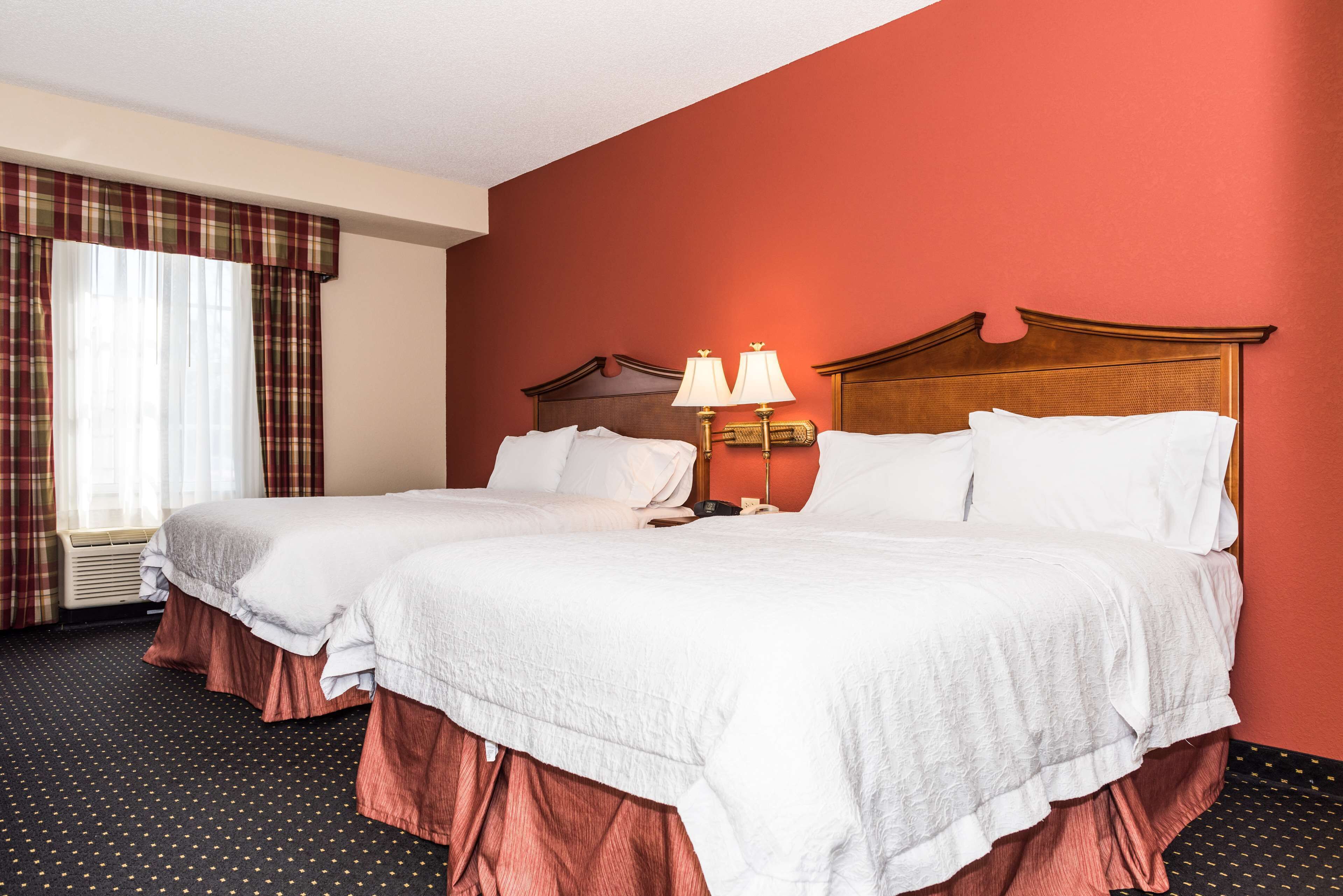 Habitación de hotel con dos camas, una pared de acento roja y una ventana con cortinas.