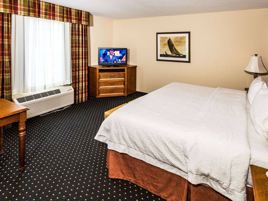 A hotel room with a bed, a desk, a television, a framed picture on the wall, and a lamp.