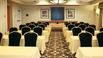 A conference room with rows of tables and chairs, a patterned carpet, and framed artwork on the walls.