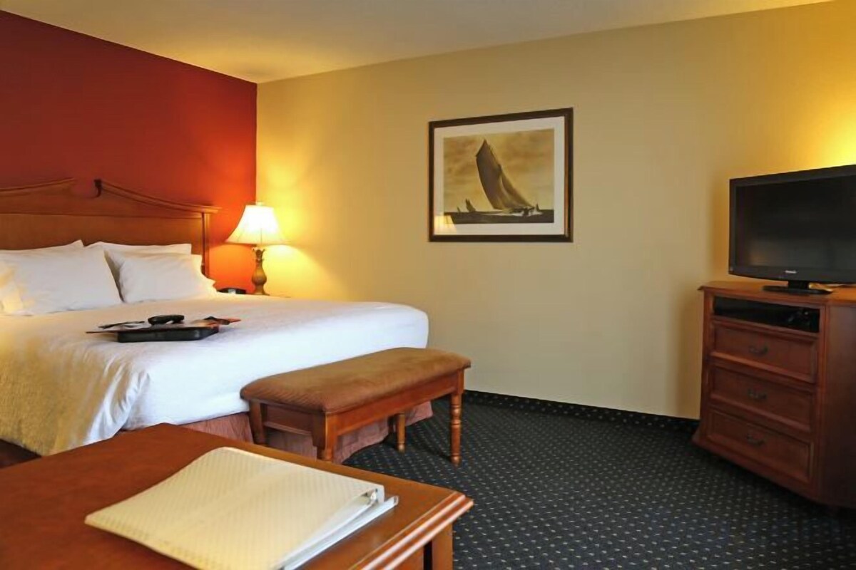 A hotel room with a bed, a desk, a television, and a painting on the wall.
