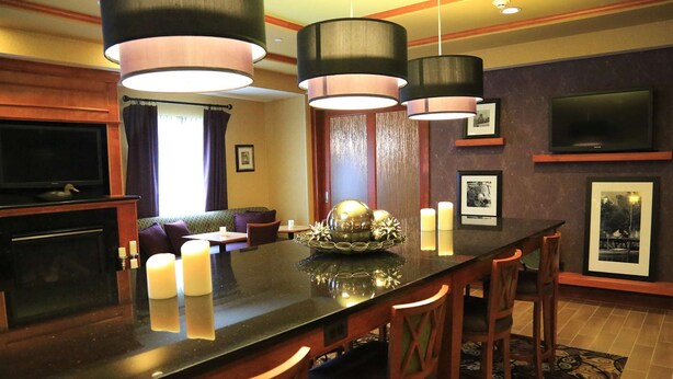 A modern hotel dining area with a long table, four chairs, and three pendant lights.