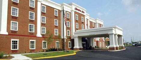 Un hotel Hampton Inn con fachada de ladrillo, varios ventanales y un acceso cubierto.