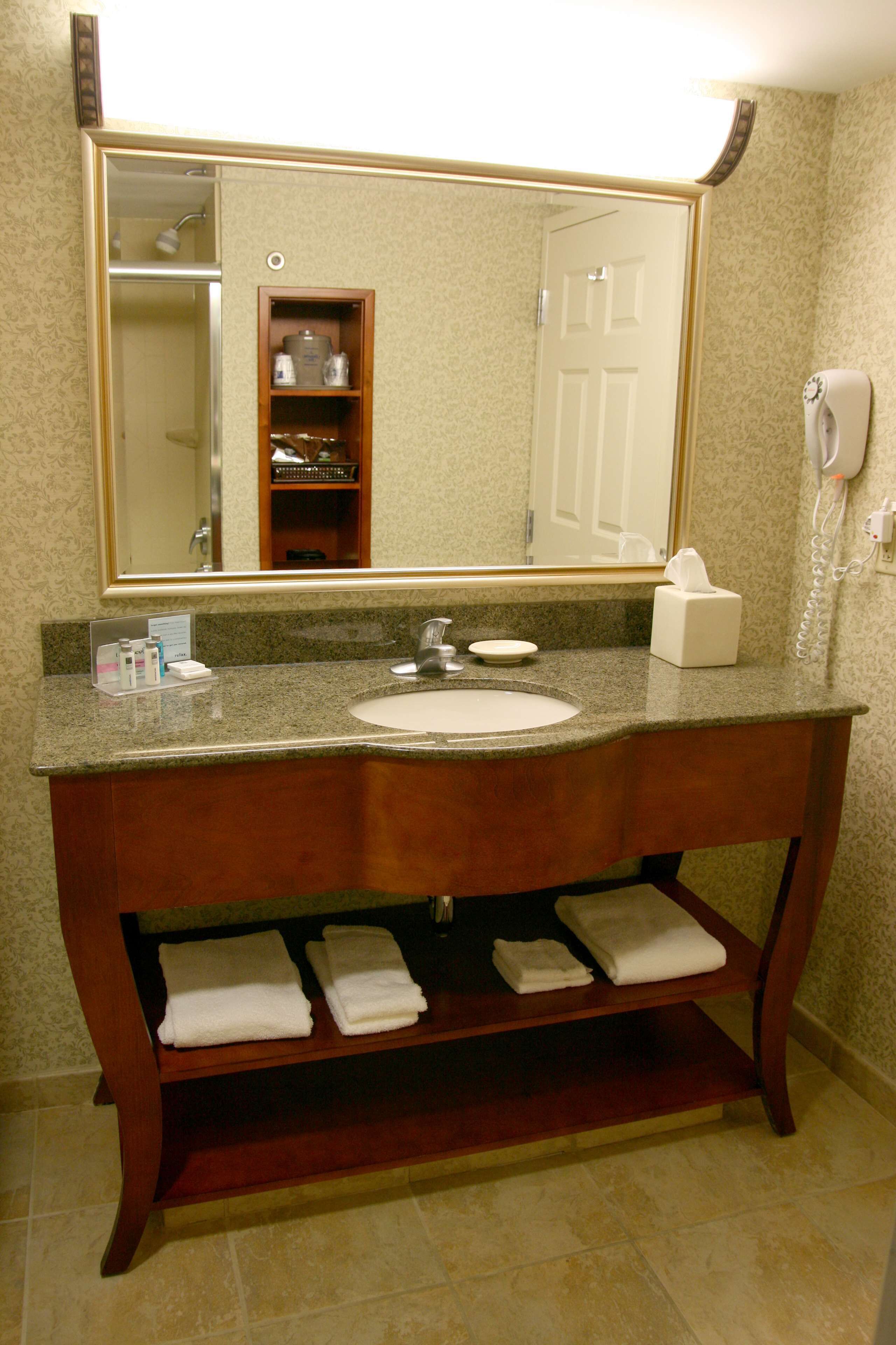 A bathroom with a granite countertop, a sink, a mirror, a towel rack, and a shower visible in the reflection.