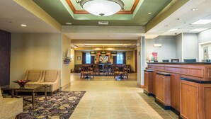 A hotel lobby with a reception desk, a dining area with chairs and a table, and a seating area with a sofa and armchairs.