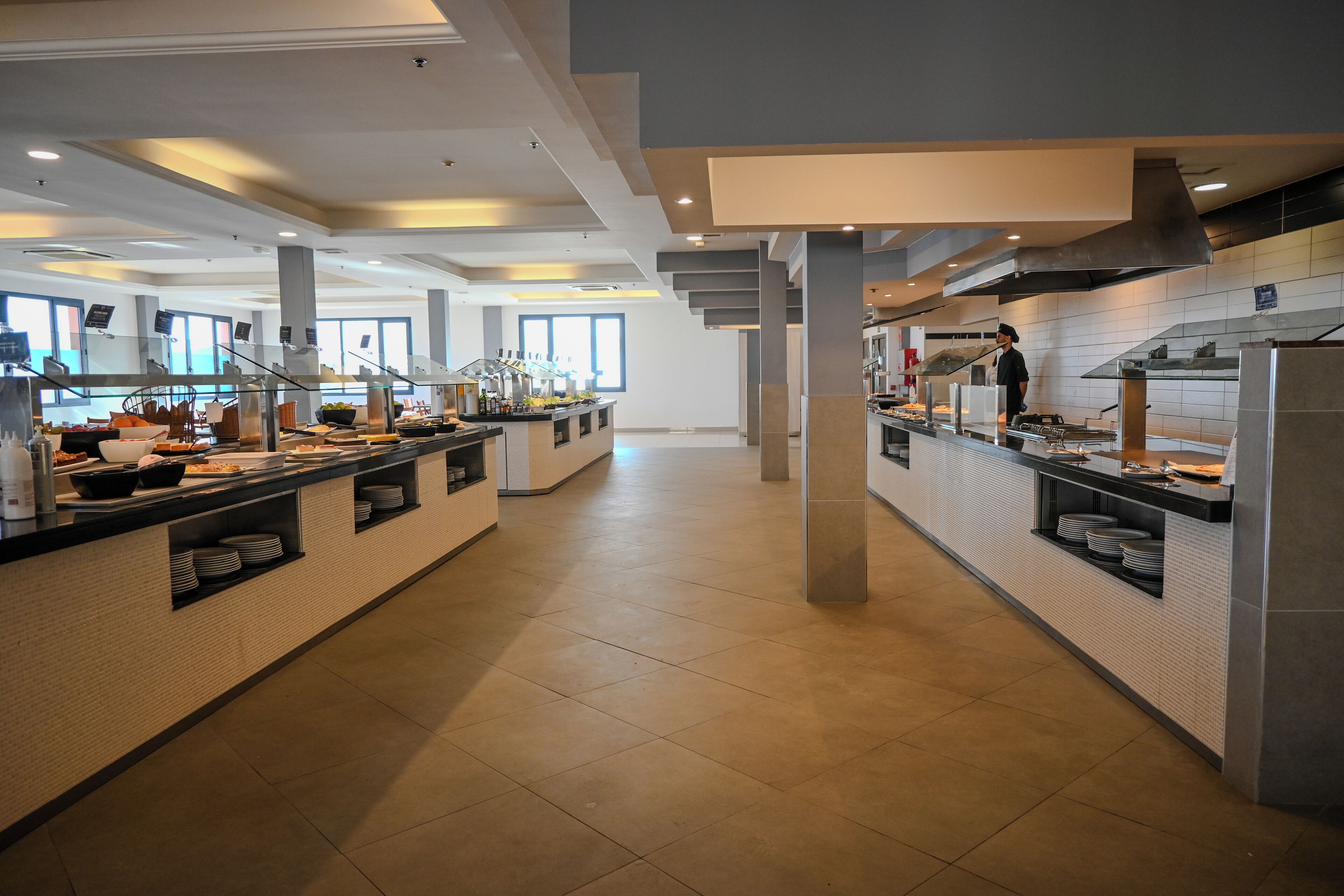 Een moderne hotelkeuken met meerdere buffetten, roestvrijstalen apparatuur en een schone, betegelde vloer.