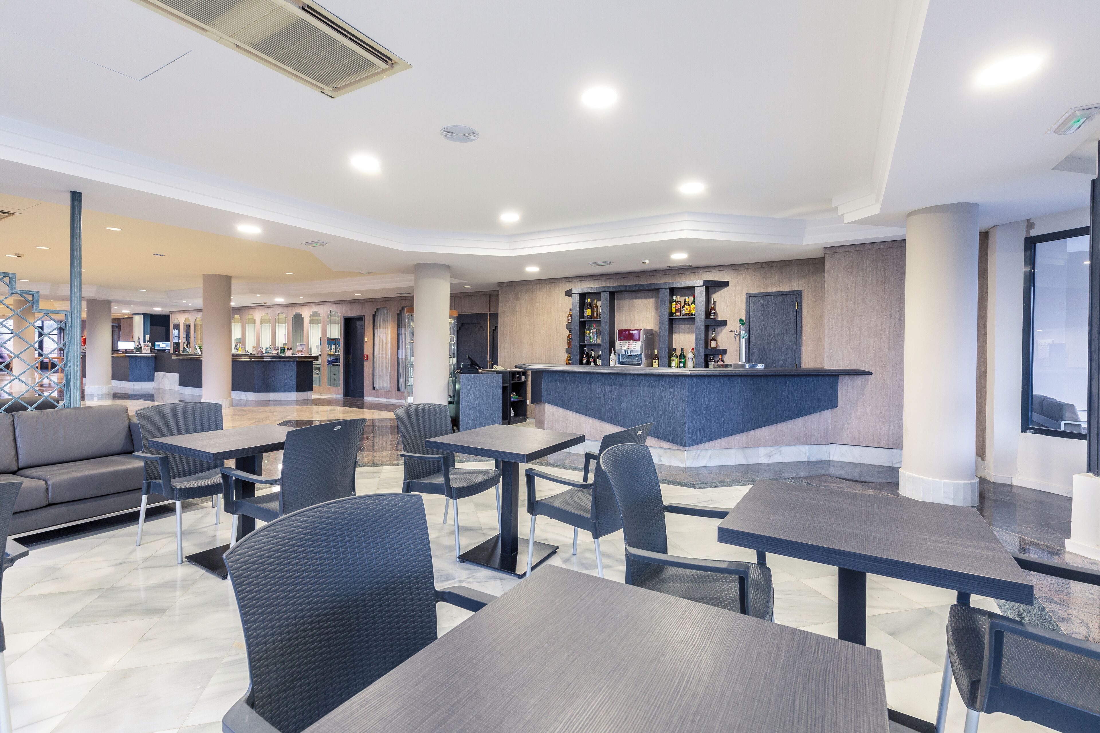 Un moderno vestíbulo de hotel con una recepción, zona de estar y un bar.