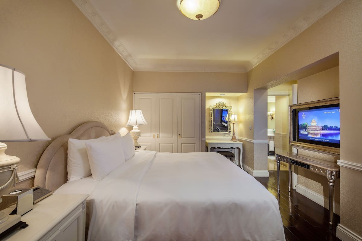 A hotel room with a bed, bedside lamps, a television, and a fireplace.
