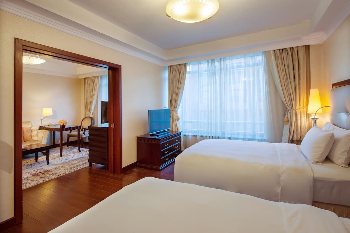 A hotel room with two beds, a TV, a desk with a chair, and a dining area with a table and chairs.