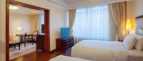A hotel room with two beds, a TV, a desk with a chair, and a dining area with a table and chairs.