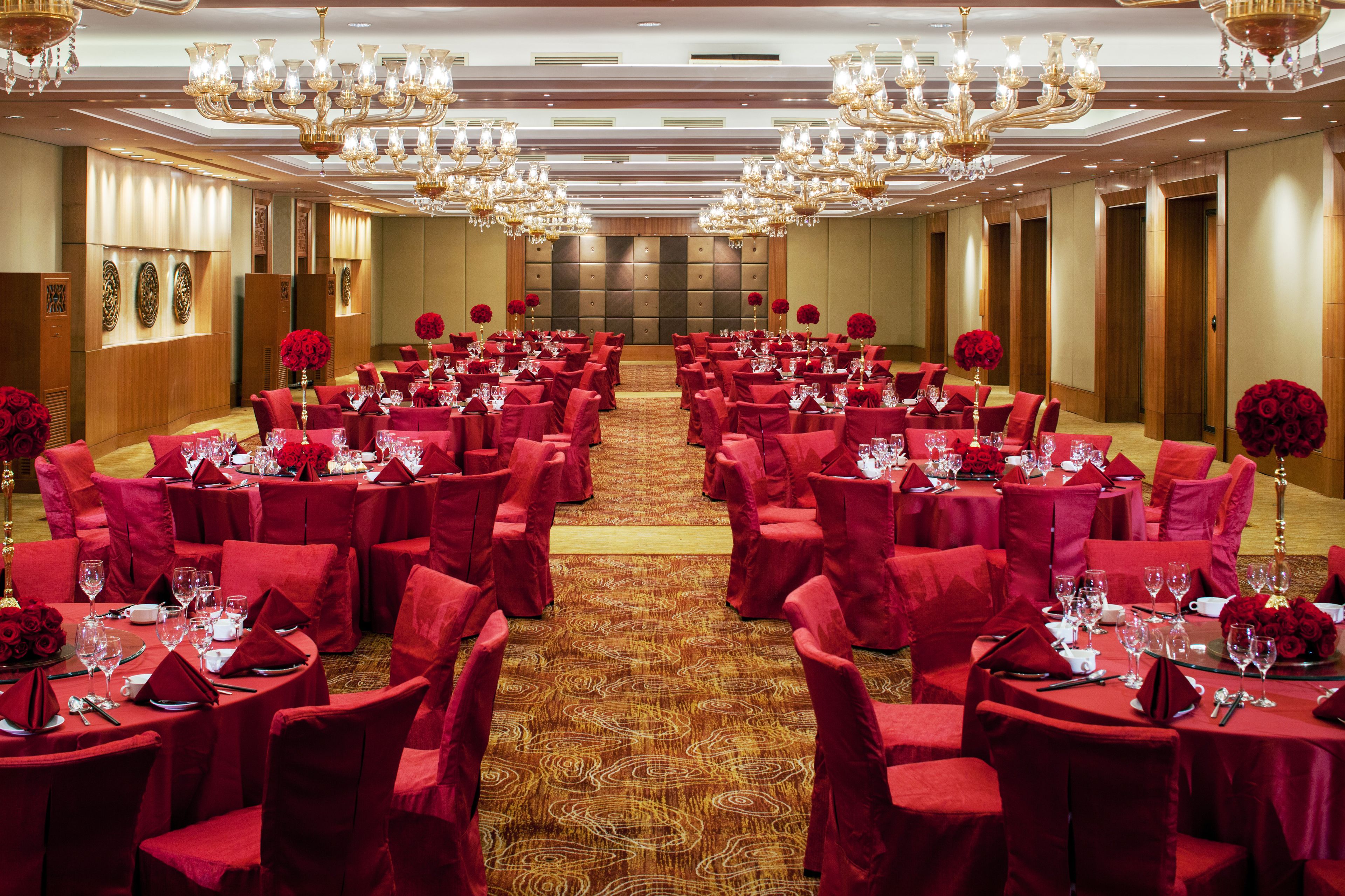 A banquet hall with round tables, red chairs, and chandeliers.
