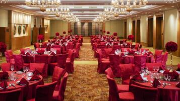 A banquet hall with round tables, red chairs, and chandeliers.