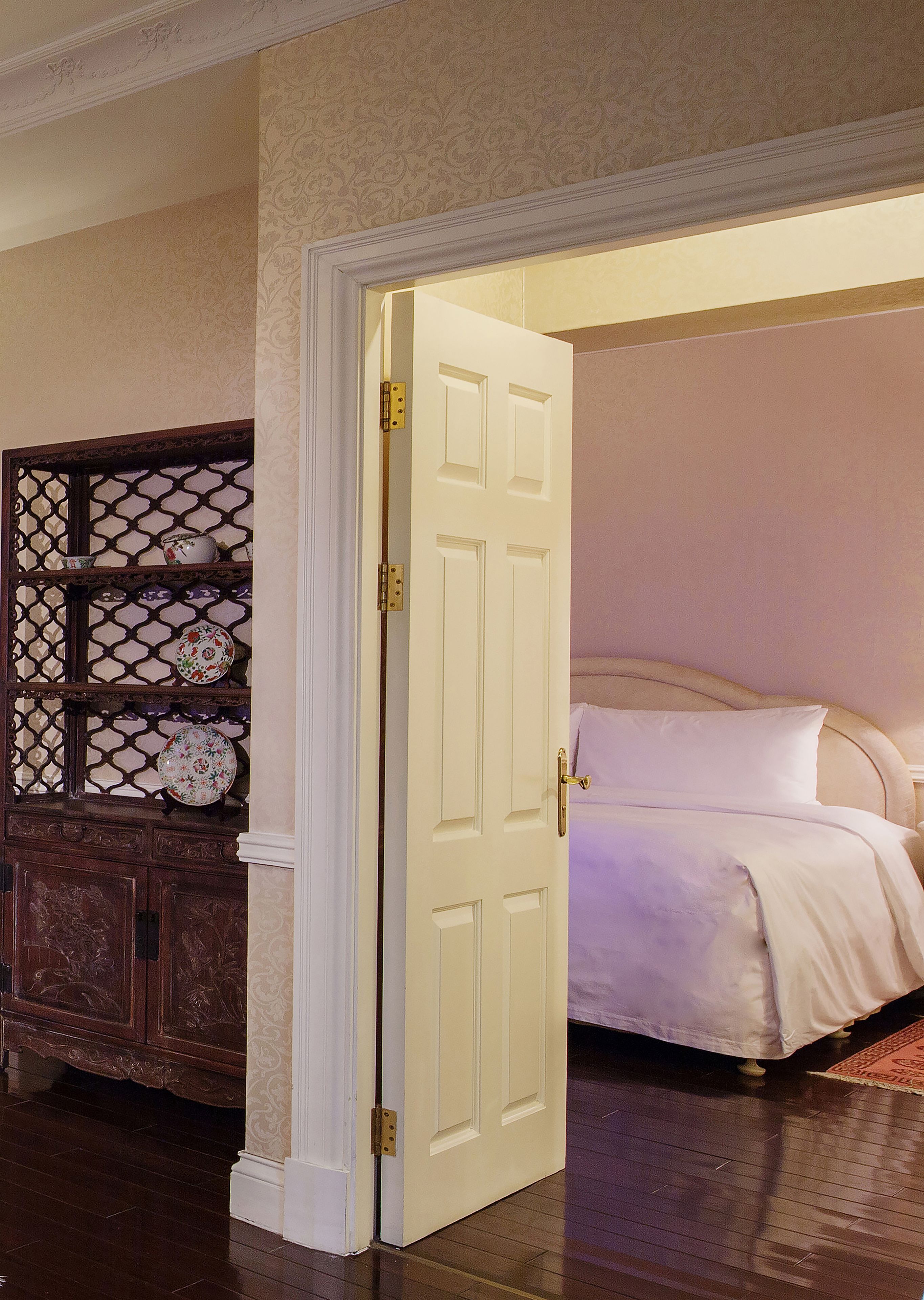 A room with a bed, a wooden cabinet with decorative plates, and a white door.