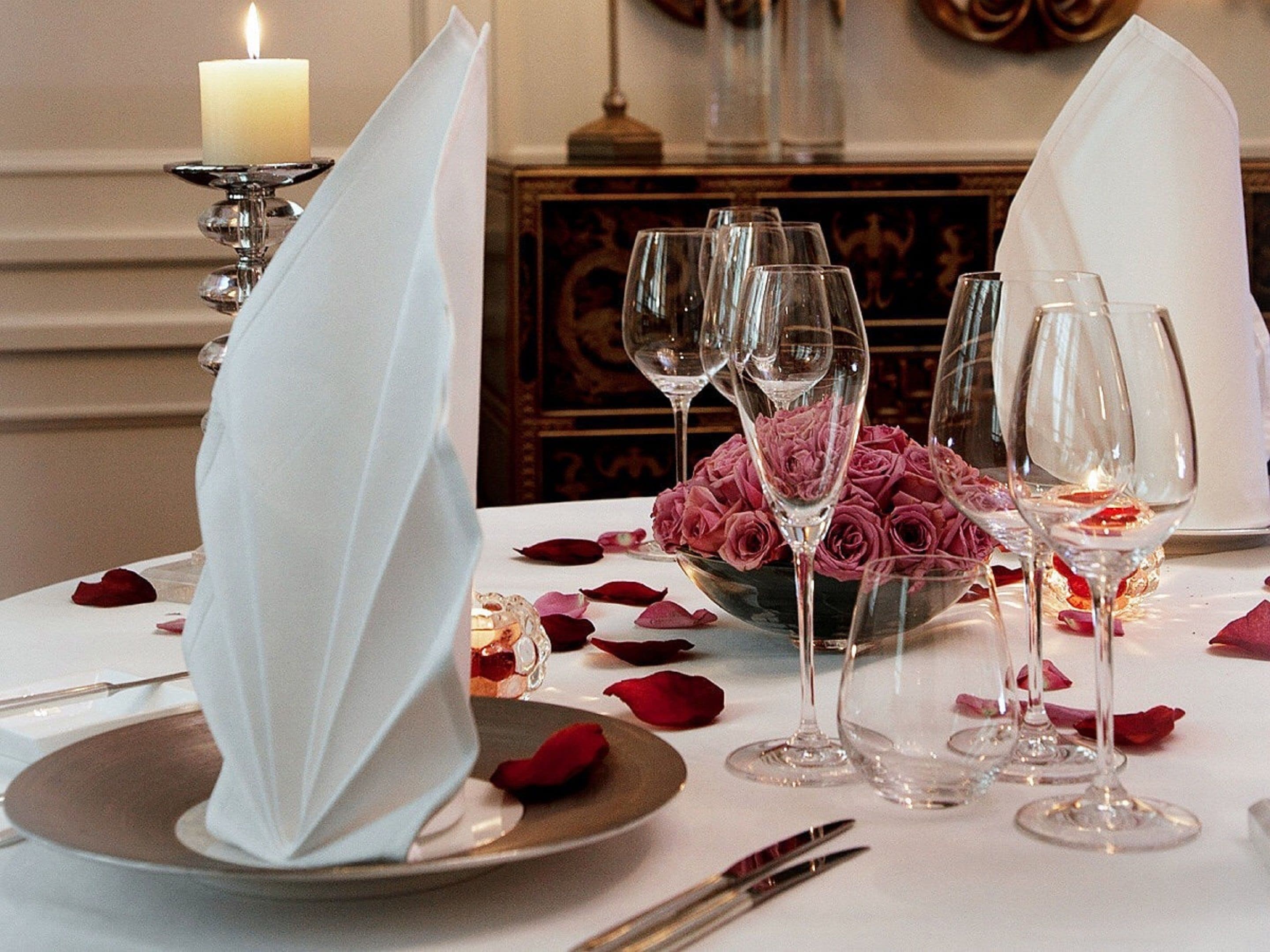 A table set for a formal dinner with a candle, wine glasses, and a bouquet of roses.