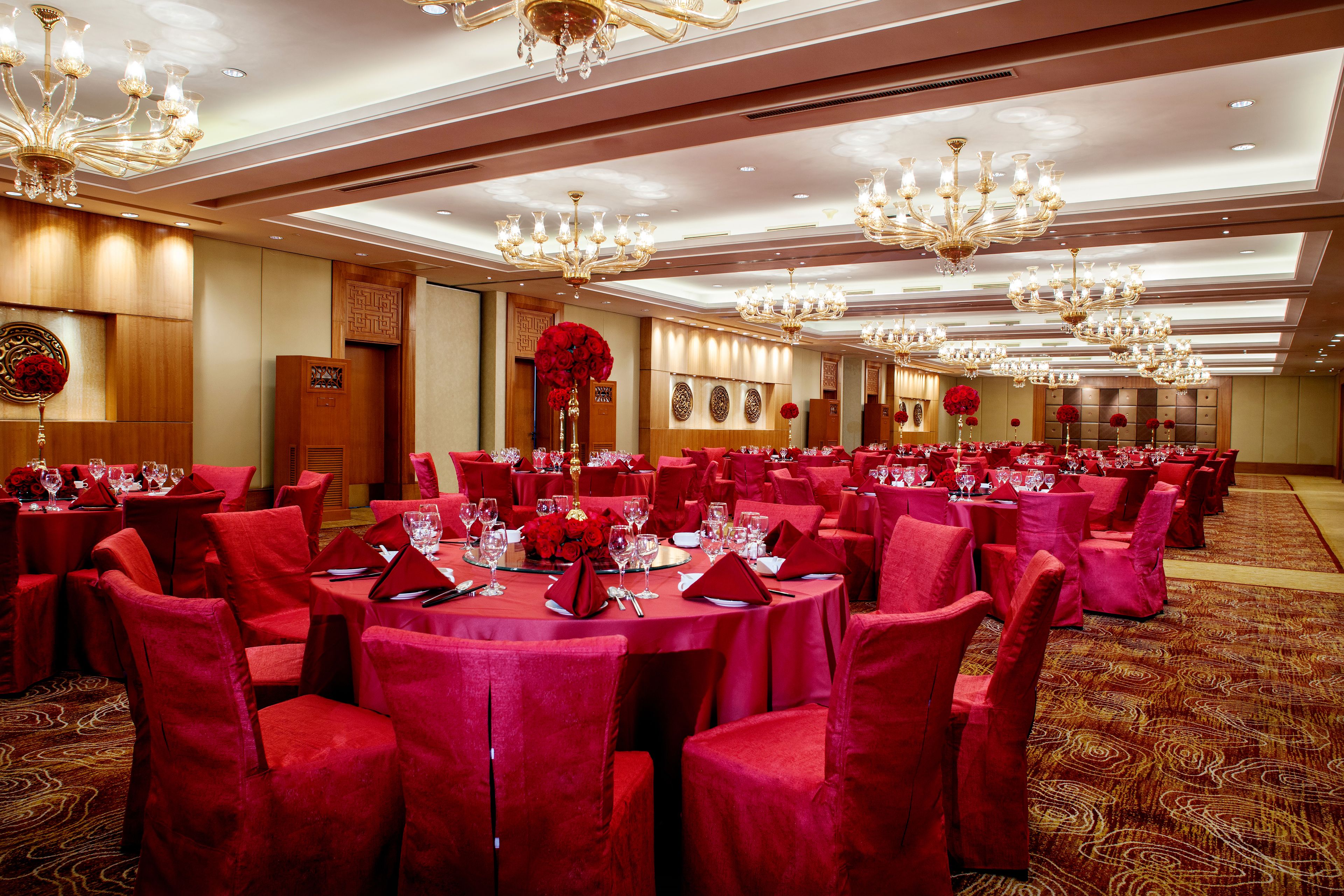 A banquet hall with round tables, red chairs, and chandeliers.