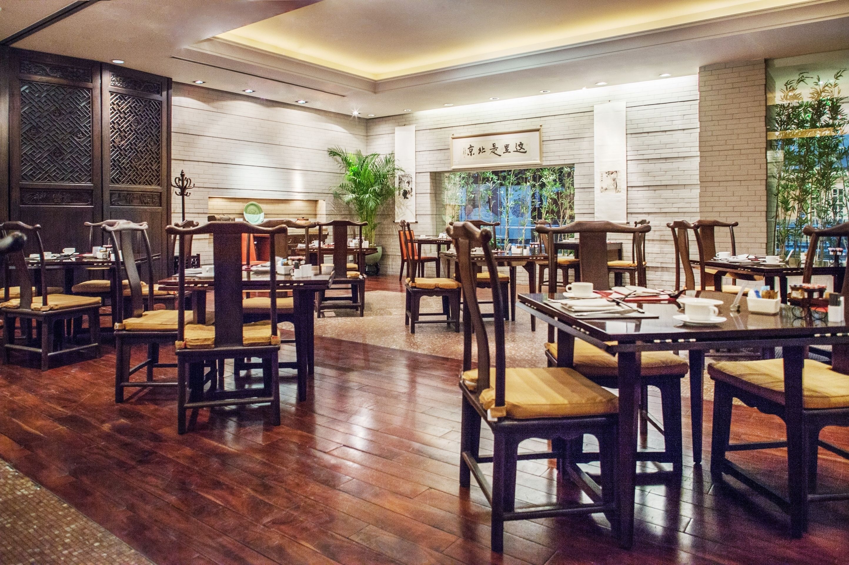 A spacious restaurant with wooden flooring and traditional wooden furniture. Tables are set with plates, cups, and cutlery.