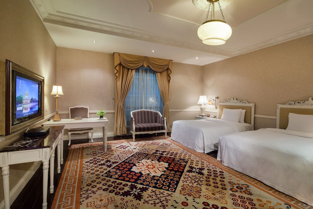 A hotel room with two beds, a desk with a television, a chair, and a patterned carpet.