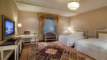 A hotel room with two beds, a desk with a television, a chair, and a patterned carpet.